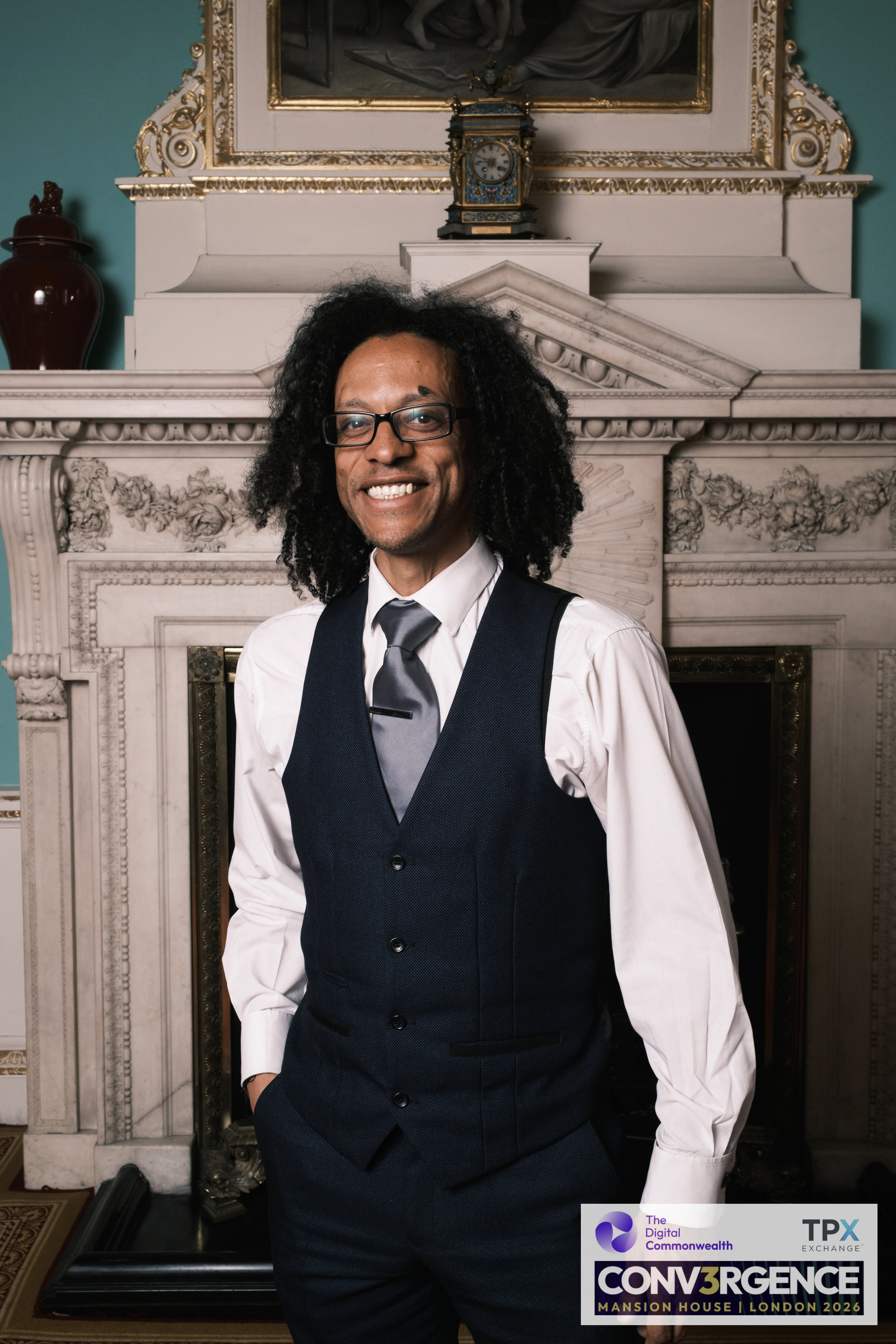 Smiling half-length portrait of JB Webb-Benjamin, hand in pocket, by the fireplace at Mansion House.