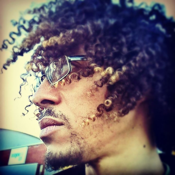 Stylised sunlit profile portrait of JB Webb-Benjamin wearing mirrored sunglasses, curly hair with blonde tips.
