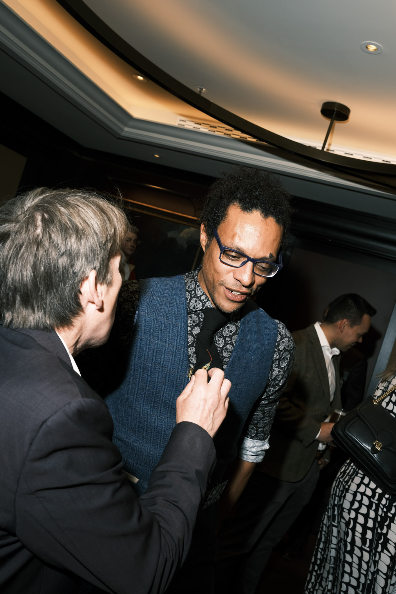 A guest reaching to look at the gold tie pins on JB Webb-Benjamin's embroidered snake tie, as JB looks down at it.